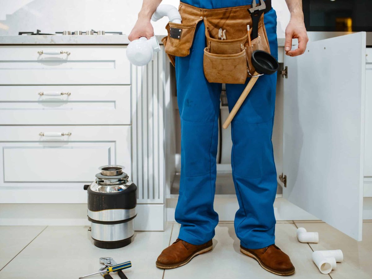 Male plumber installing water filter in the kitchen. Handywoman with toolbag repair sink, sanitary equipment service at home